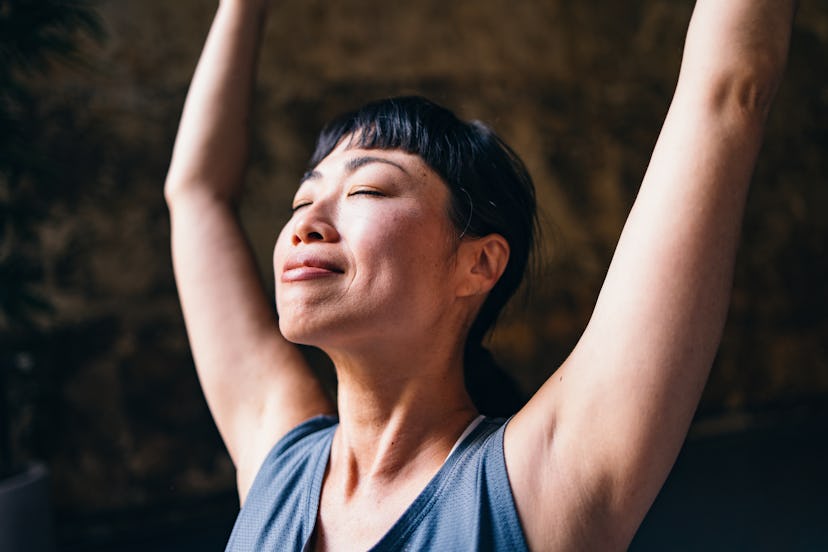 Smiling Asian woman in sportswear stretching her arms at the yoga studio.