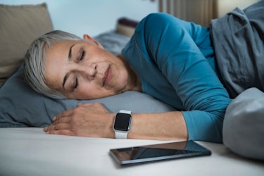 Sleep Apps - Tech-savvy Senior Woman Sleeping in Bed, Using Smart Phone and Smart Watch to Improve h...