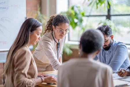 A young mature adult leads a small group of business professionals in a meeting. They are each dres...
