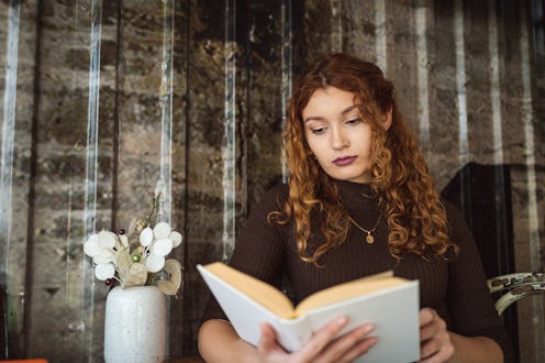 Young Caucasian woman reading book, at the modern coffee shop