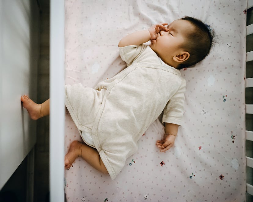 Cute Asian baby girl sucking thumb while sleeping peacefully in baby cot