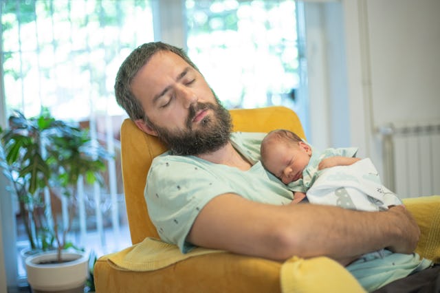 Portrait of father and a newborn baby sleeping in an armchair in their living room.