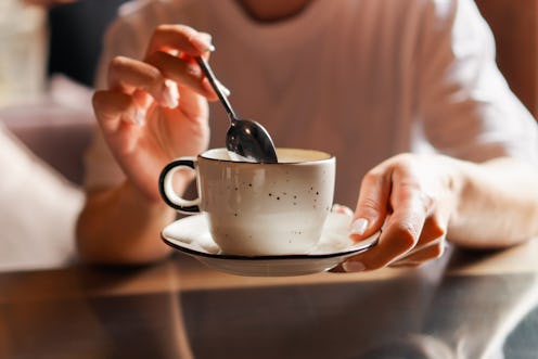 Closeup of female hands with french manicure holding cozy ceramic white mug of tea or coffee. Relax ...