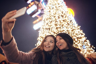 Smiling girlfriends taking a selfie and use pine tree puns as christmas tree jokes on Instagram.