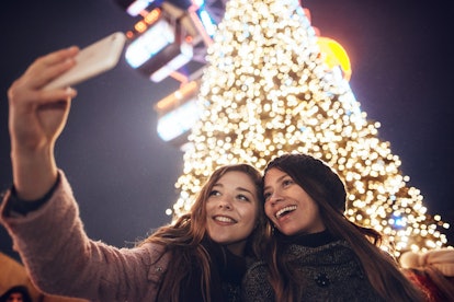 Smiling girlfriends taking a selfie and use pine tree puns as christmas tree jokes on Instagram.