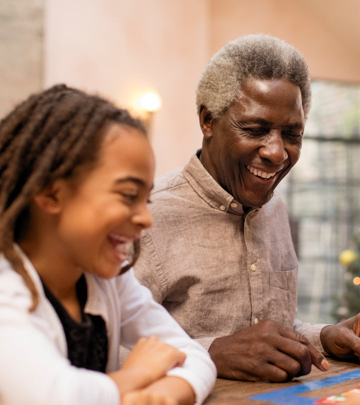 A grandfather and young granddaughter sitting next to each other at the table for a holiday meal, go...
