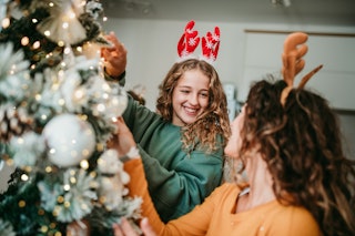 A girl is decorating the Christmas Tree with her mum. She is happy to spend the winter holidays with...