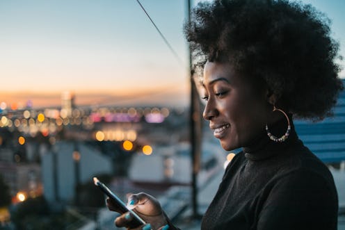 A silhouette of an African woman with curly hair looking at her phone during blue hours outdoor