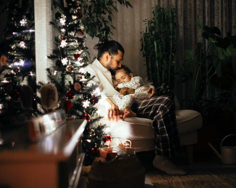 Young girl falls asleep on father's lap in her bedroom decorated for Christmas.