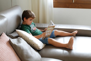 An introverted kid sitting on the couch reading a book