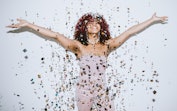 A young woman, dopamine dressed in a sparkling gown for the 2022 holidays, throws confetti in the ai...