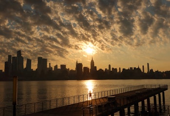 HOBOKEN NJ - AUGUST 4: The sun rises behind the Empire State Building in New York City as a woman ru...