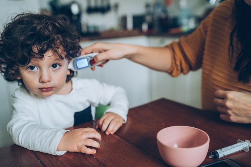 Mother with ear thermometer checking temperature in an article about day care sickness and day care ...