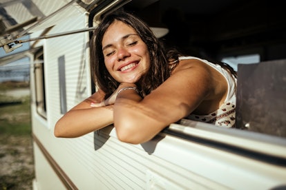young woman rests arms on RV window as she smiles and thinks about how the november 2022 new moon wi...