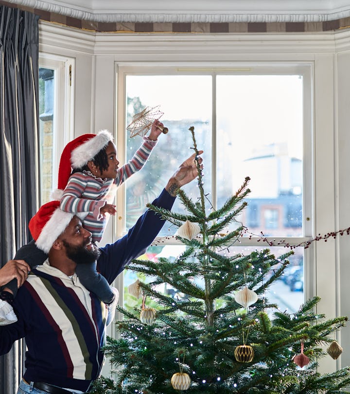 Father and daughter decorating Christmas tree in an article about can christmas trees catch fire?