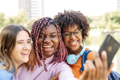 A group of three teenage friends smile and press together for a selfie on a bright spring day. Your ...