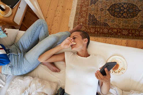 Directly above view of cheerful young woman looking at female friend sitting on bed at home