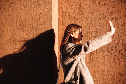 young woman reaches out her hand to block sunlight from hitting her face, as she considers the spiri...