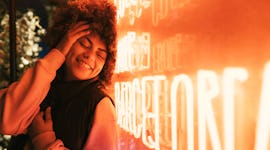 A young woman rests her head on a neon sign as she considers the December 2022 full Cold Moon's spir...
