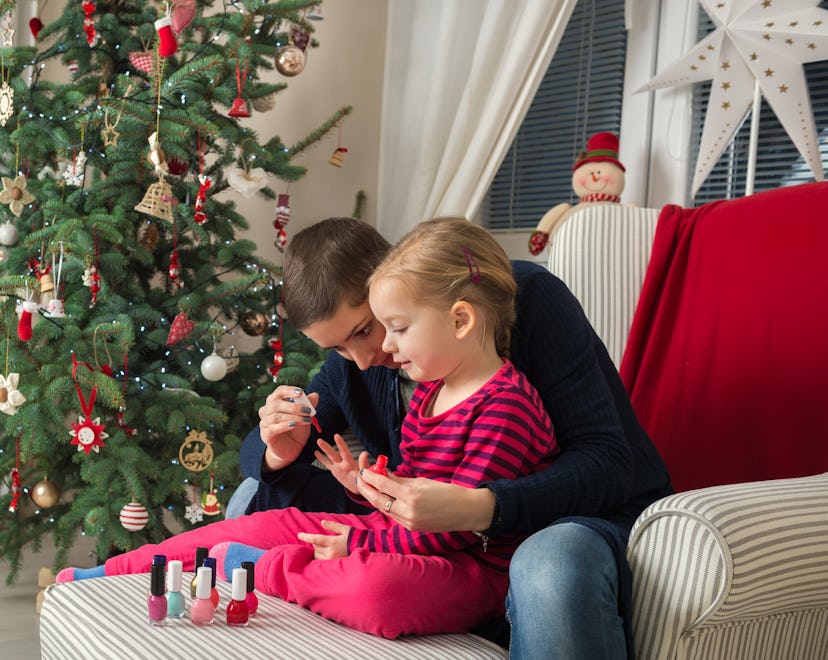 A mom and daughter paint mommy-and-me holiday nails at home next to the Christmas tree.