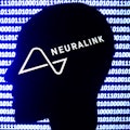 Neuralink logo displayed on a phone screen, a silhouette of a paper in shape of a human face and a b...