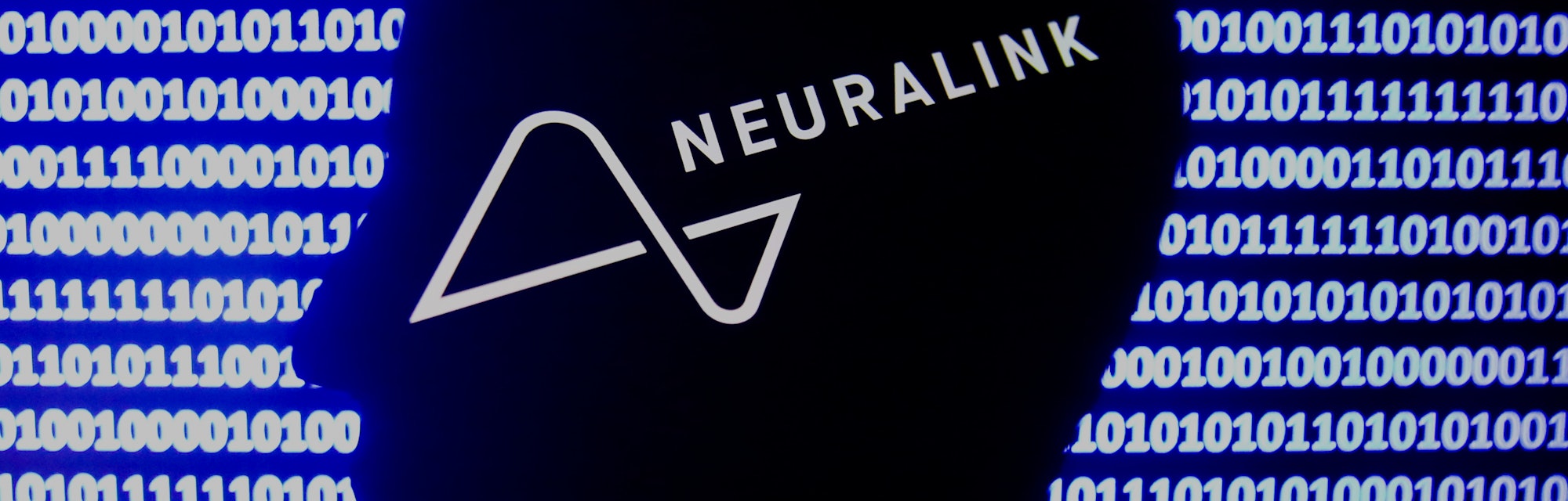Neuralink logo displayed on a phone screen, a silhouette of a paper in shape of a human face and a b...