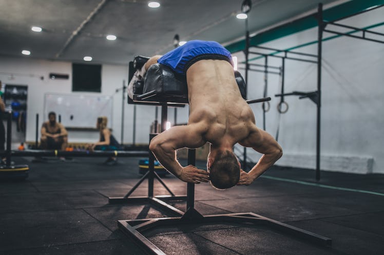 Athlete doing low back exercise on roman bench while two people are resting behind him