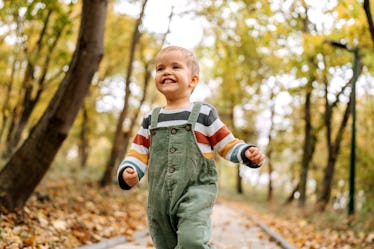 Portrait of cute little smiling boy running in a public park