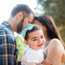一个快乐的拉丁女婴在她父母的怀里微笑着在一个水平的腰上拍摄户外。