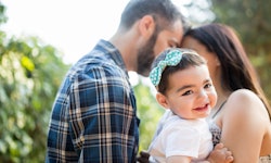 一个快乐的拉丁女婴在她父母的怀里微笑着在一个水平的腰上拍摄户外。