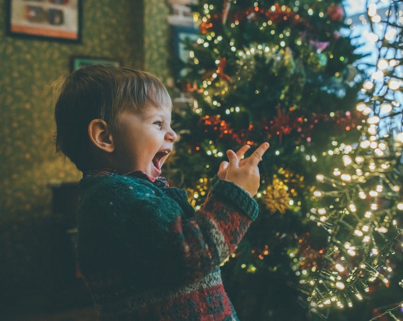 Little boy in Christmas sweater excitedly points at lights going on the Christmas tree