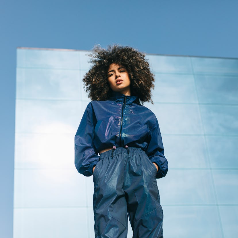 a young woman poses in front of a blue brick wall and gazes into camera, as she considers the spirit...