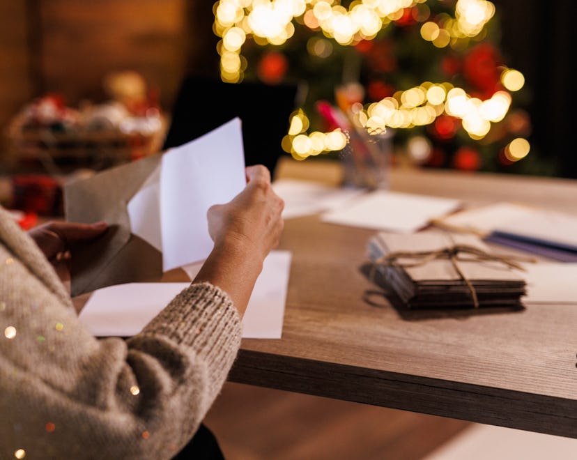 Close up shot of a person putting a Christmas card in an envelope, sitting in front of a decorated C...