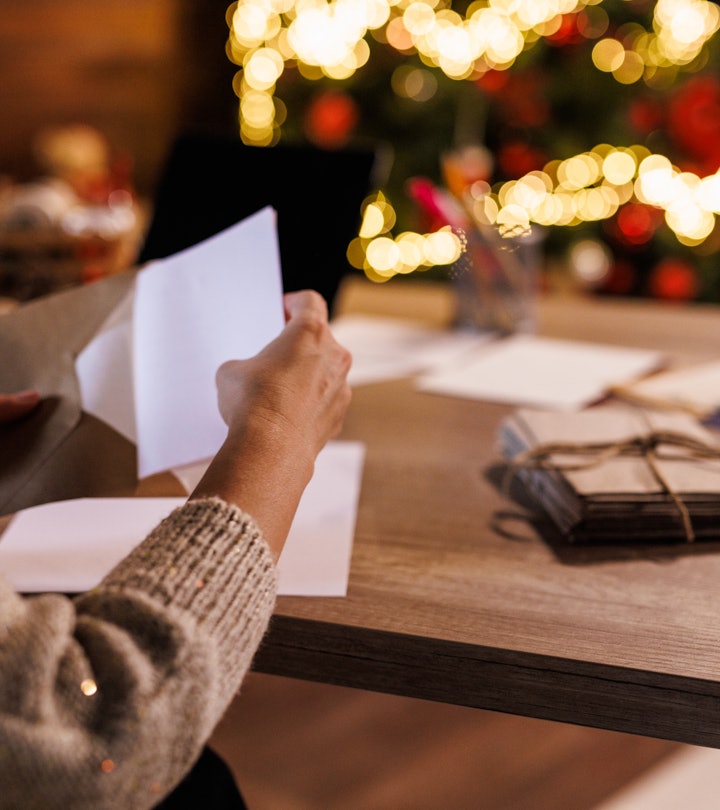 Close up shot of a person putting a Christmas card in an envelope, sitting in front of a decorated C...
