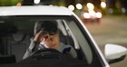 担心的亚洲商人晚上开车上班时用智能手机工作，他觉得很累