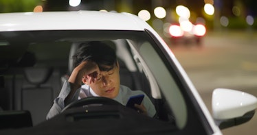 Worried asian businessman use smart phone to work while commuting in car at night - he feels tired
