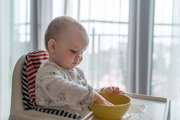Baby sits in a high chair and fooling around with a bowl at the dinner table.