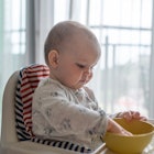 Baby sits in a high chair and fooling around with a bowl at the dinner table.