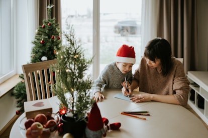 A mother and son sitting at a table at home at Christmastime, figuring out what to write in a Christ...