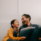 Father and young daughter reading book together at home
