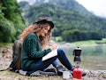 A beautiful solo traveler outdoors in nature writes in her journal, which is one of the best travel ...