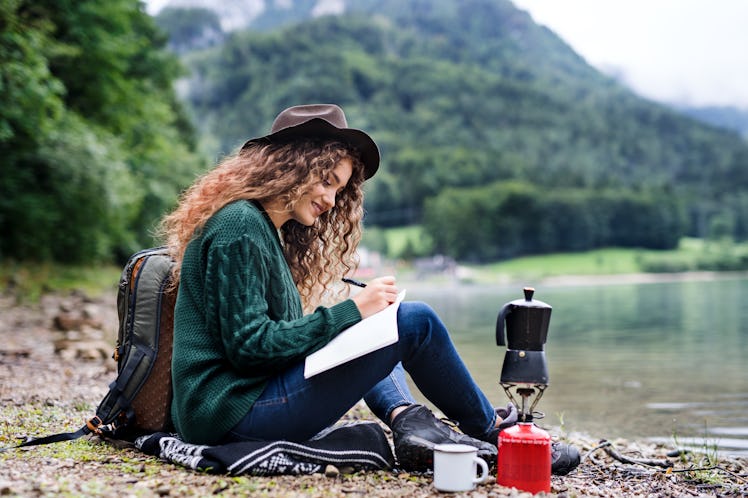 A beautiful solo traveler outdoors in nature writes in her journal, which is one of the best travel ...