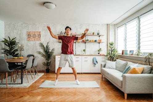 一个年轻英俊的中国男人在家里锻炼。在家做开合跳运动。