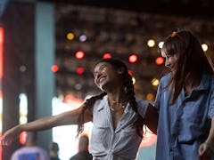 Two girlfriends of Asian and Caucasian ethnicity are dancing in front of the stage and enjoying the ...