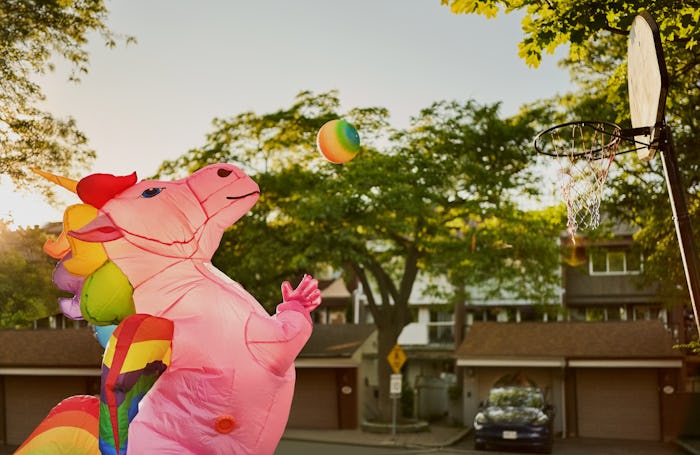 Person wearing an inflatable unicorn costume playing basketball on street court outdoors on a sunny ...