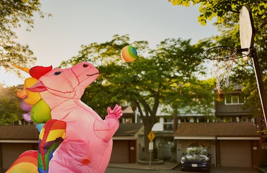 Person wearing an inflatable unicorn costume playing basketball on street court outdoors on a sunny ...