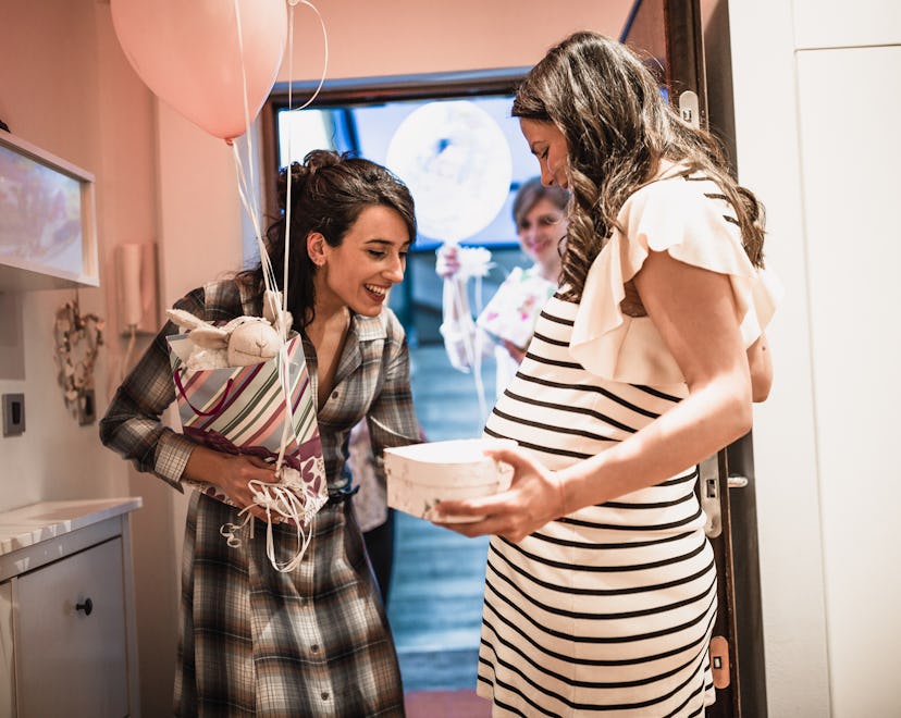 Pregnant woman welcoming her girlfriends on the doorway, bringing her a thoughtful, lovely gift for...