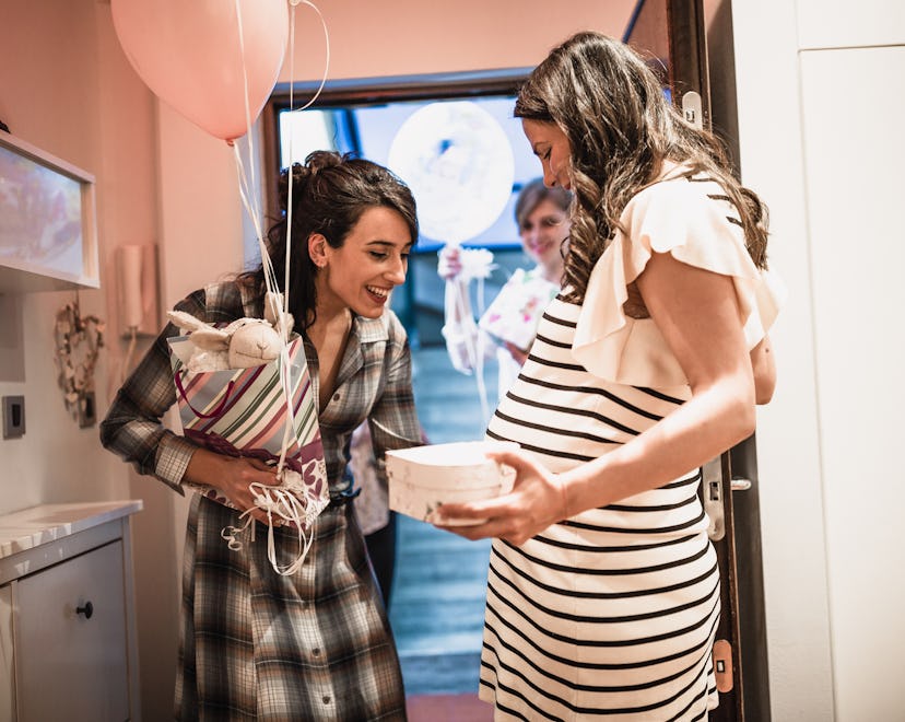Pregnant woman welcoming her girlfriends on the doorway, bringing her a thoughtful, lovely gift  for...