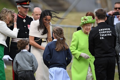 WIDNES, ENGLAND - JUNE 14:  Queen Elizabeth II looks on as Meghan, Duchess of Sussex receives flower...