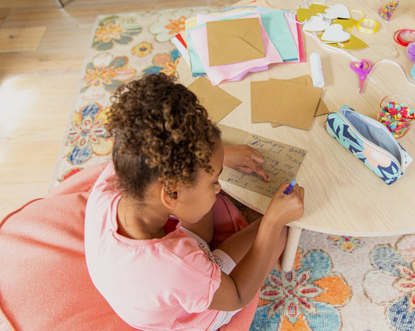 Young girl sitting at the table in her house making a kids thank you card